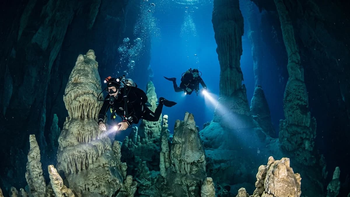 Mergulhadores de cilindro profissionais explorando as gigantescas colunas e cones de calcário submersos no lago azul subterrâneo do Abismo Anhumas em Bonito MS