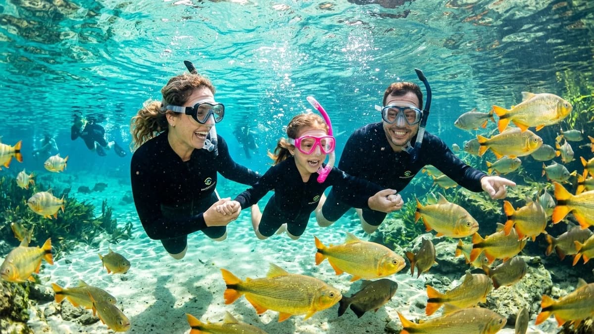 Família de ecoturistas sorrindo e flutuando de mãos dadas nas águas turquesa da Nascente Azul em Bonito MS cercada por cardumes de peixes coloridos