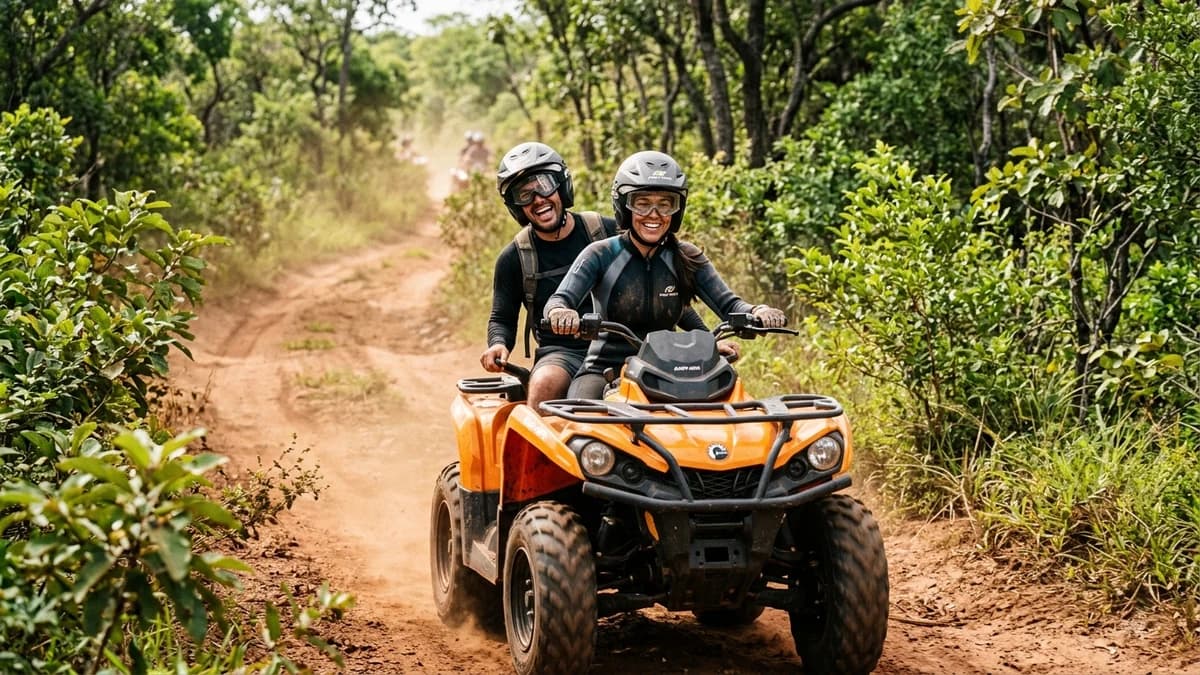 Casal de ecoturistas sorrindo e pilotando um quadriciclo rústico em dupla na Trilha Boiadeira em Bonito MS vestidos com capacete e óculos em meio à vegetação do cerrado